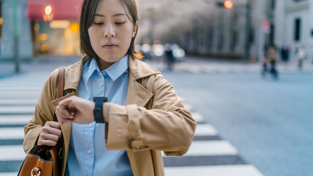 Woman walking across the street looking at her watch