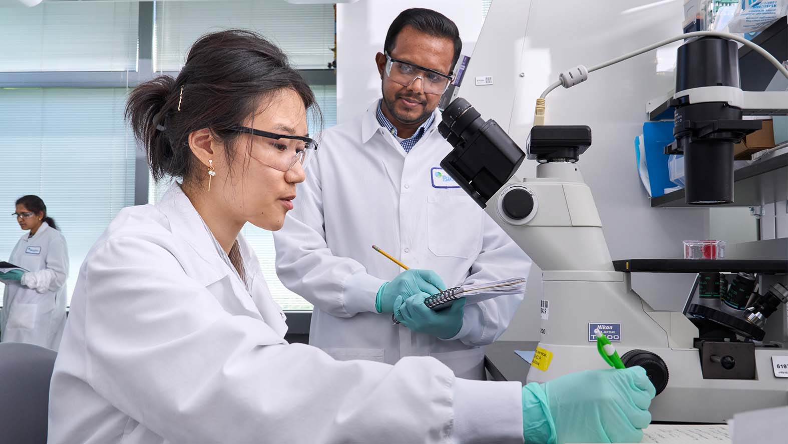 Two Biogen scientists working in the lab using a microscope