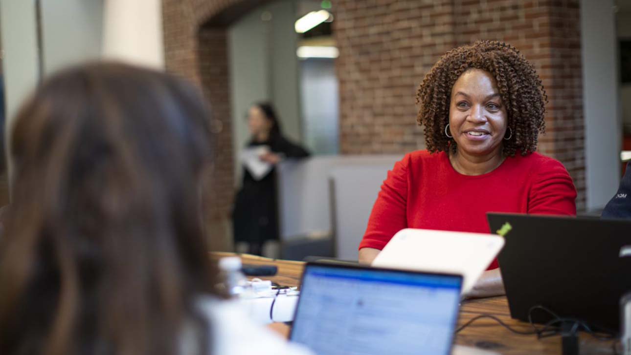 Cherie Butts, Ph.D., Medical Director and Head of Human Biology Research at Biogen, sitting at desk and talking to someone