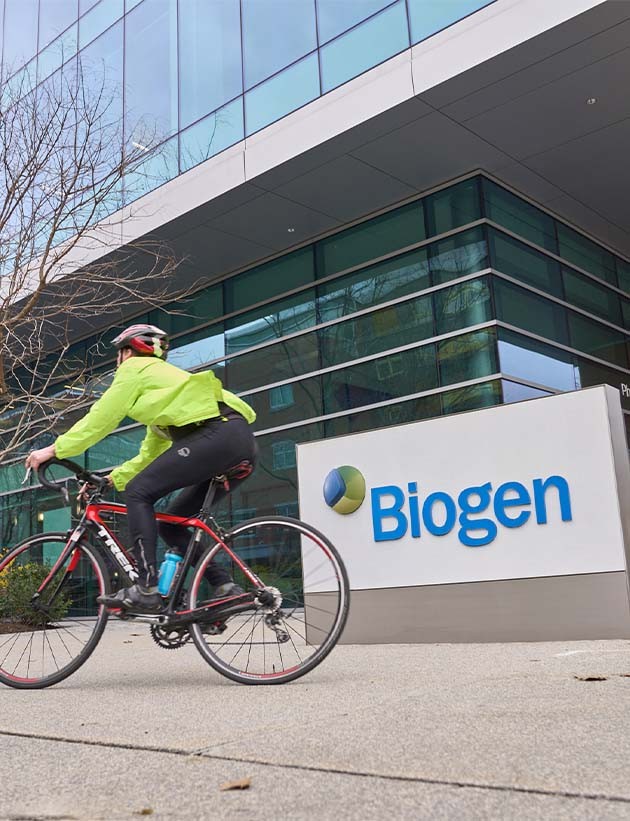 Man riding a bicycle past a Biogen sign