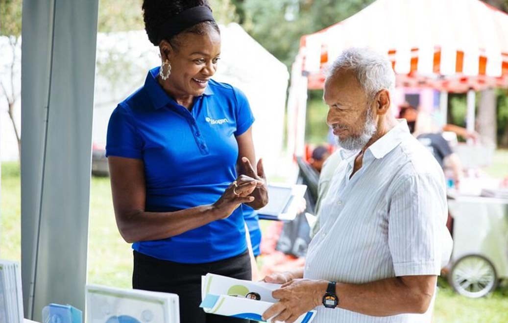 Woman in Biogen shirt talking to a man who is holding some paperwork